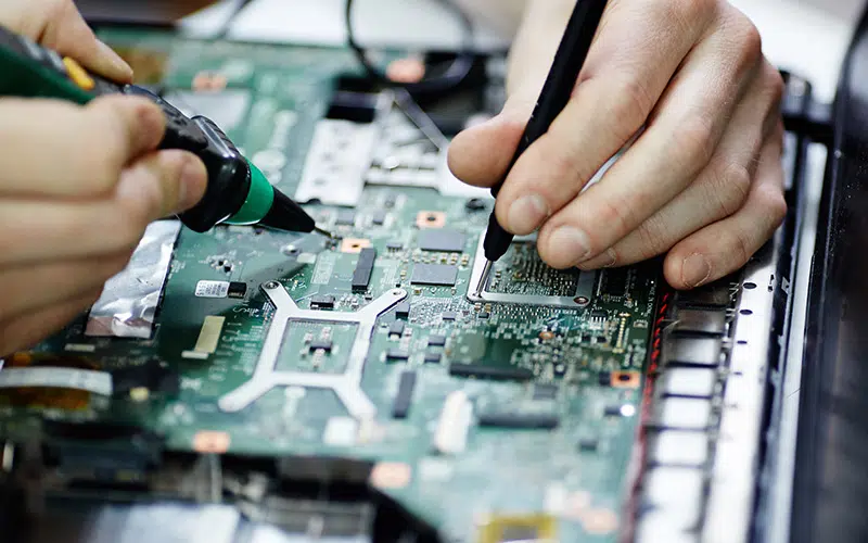 AURA-solder-PCB-AdobeStock_136939755-800×500 Gros plan sur les mains d'une personne utilisant un fer à souder sur un circuit imprimé.